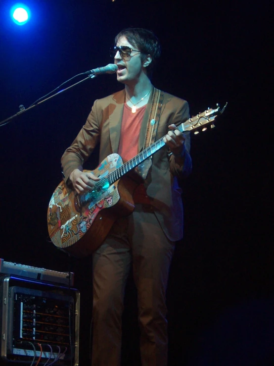 man in a tuxedo singing into a microphone with a guitar