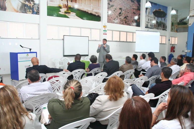 an audience sitting in white chairs are watching the presentation