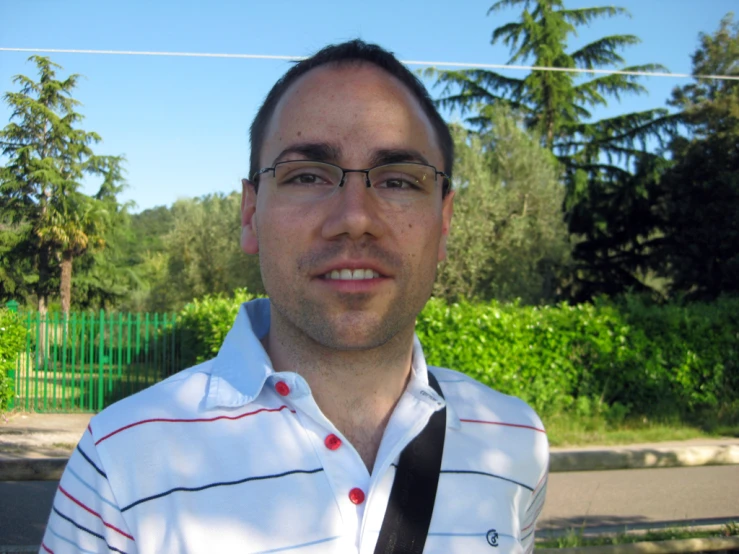 a man in glasses and shirt with a tie in front of some trees