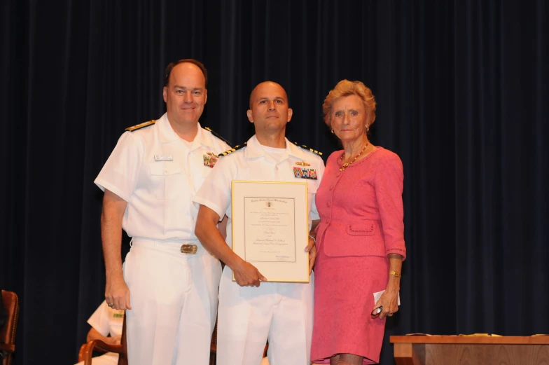 two men in dress uniforms and a woman standing beside a man wearing a white suit