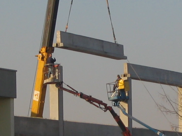 a construction worker sits on a cherry picker while a man stands under a large sign in the air