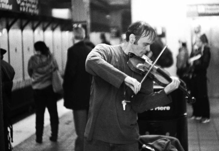a man playing violin in an station with people walking on either side