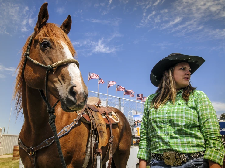 a girl is standing by a brown horse in front of flags and a blue sky