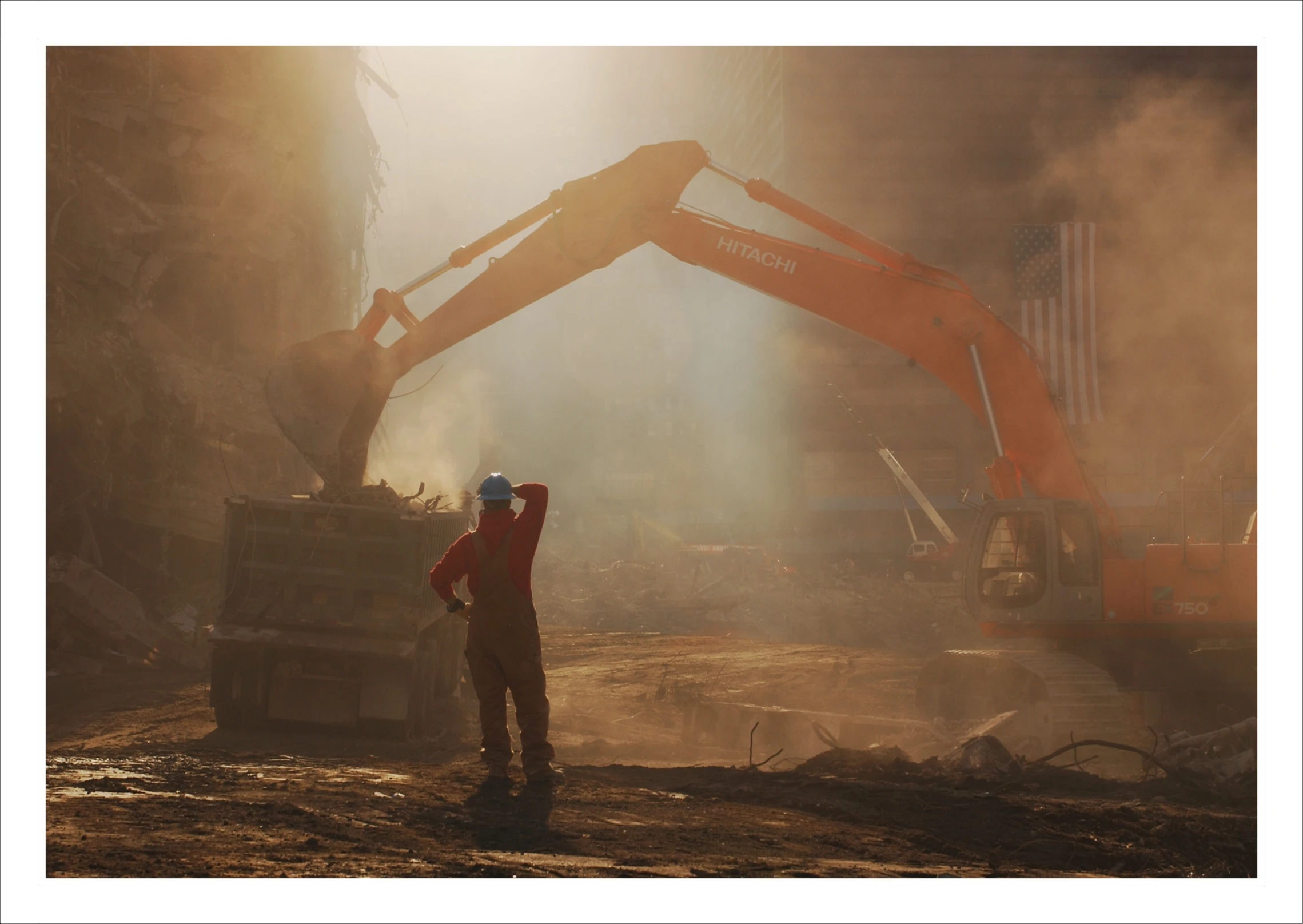 man standing at the top of a dumpster truck near a construction site