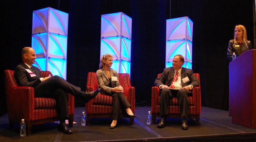 three people sitting in red chairs in front of a speaker