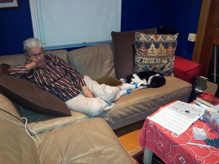 an older woman with glasses and a cat sleeping on a couch