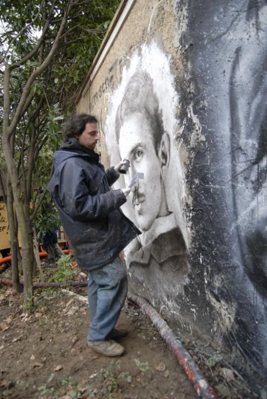 a man in blue jacket painting on wall with grey and black drawing