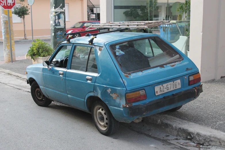 an old blue hatchback car with luggage on top
