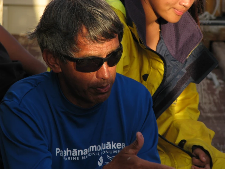 an old man with sunglasses on sitting next to a young woman