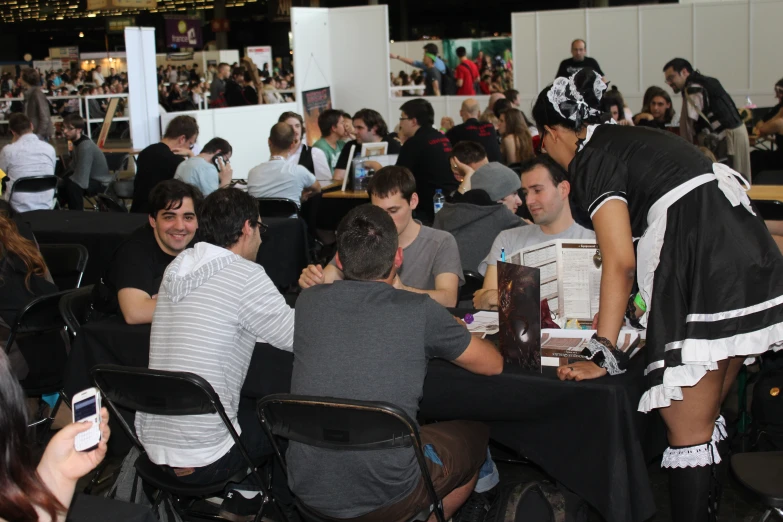 a large group of people sitting at tables with a table cloth on top