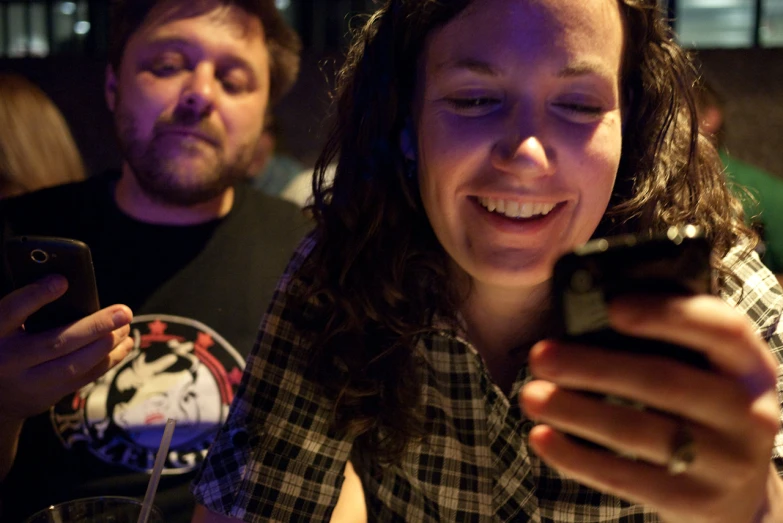 a man and woman looking at their phones while one man is smiling