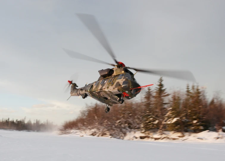 a large army helicopter flying over a snow covered slope