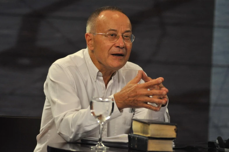 a man sits at a table with a book and glasses in front of him