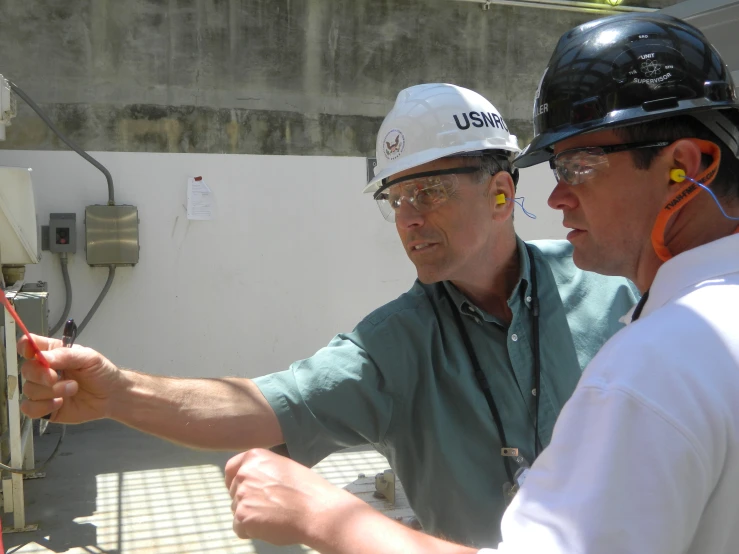 two men in hard hats are holding some wires