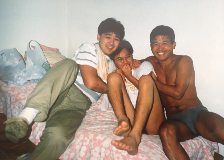 three people are smiling and sitting on a bed