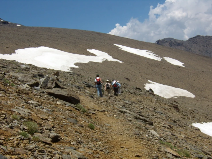 three hikers ascending up a rocky mountain on a sunny day