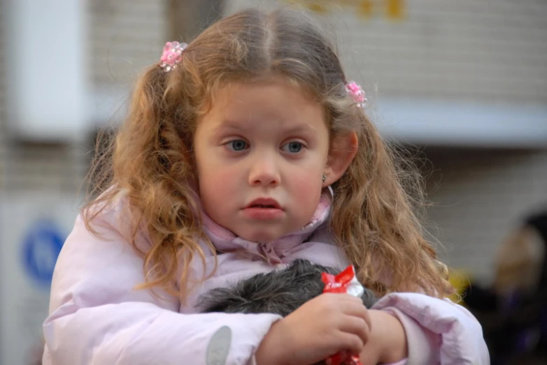 a little girl holding a teddy bear while sitting on a park bench