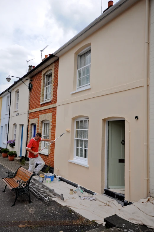 a woman in red shirt painting a house next to a road