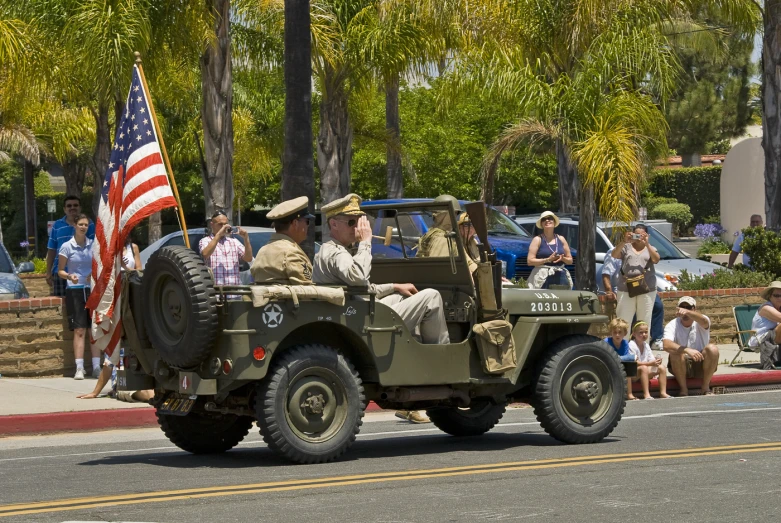 a large jeep drives through the street with a group of people watching