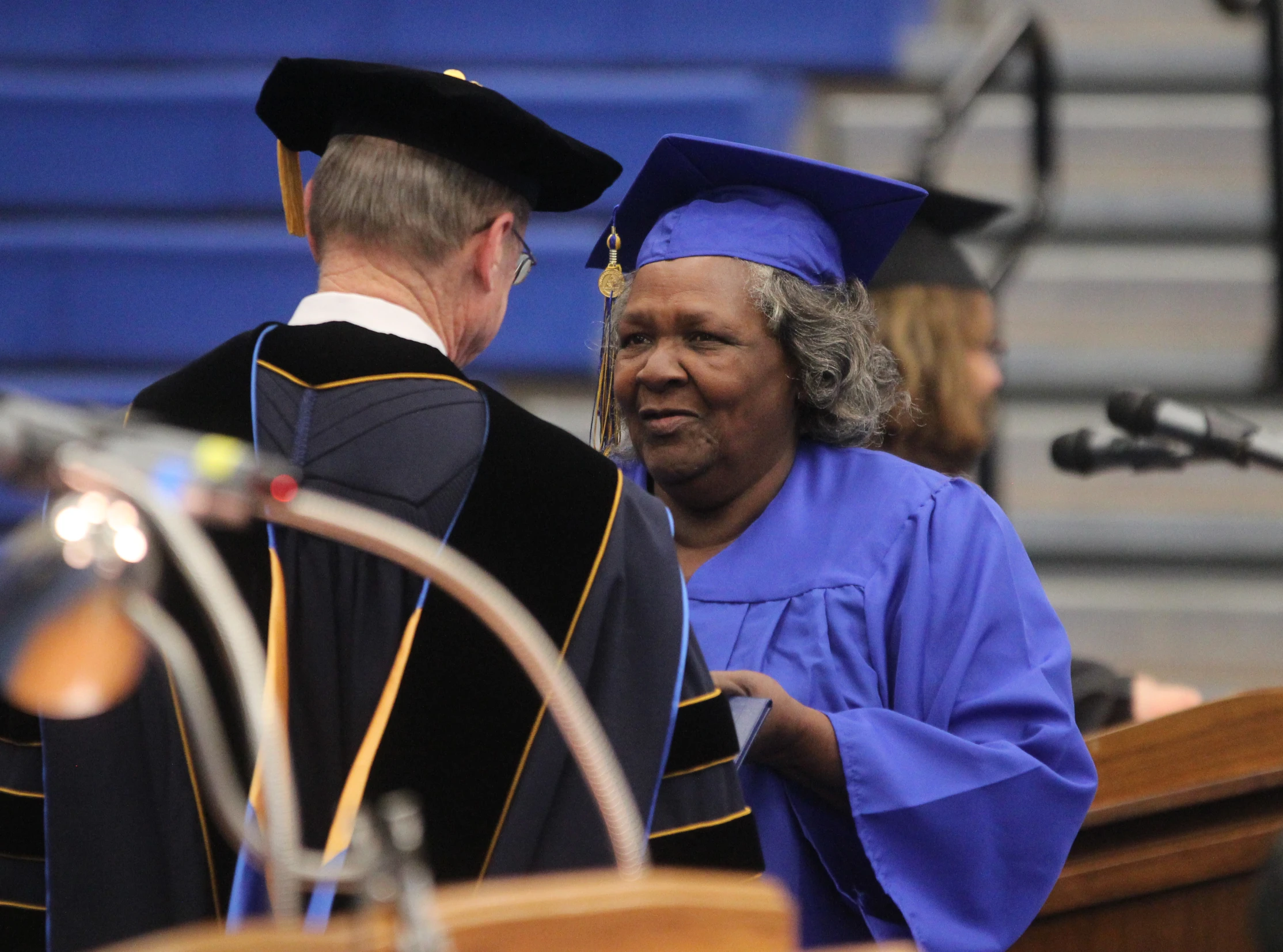 a man in a graduation gown is shaking hands with an older person