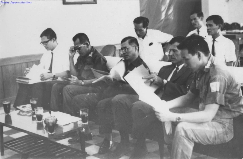 black and white pograph of nine men sitting at coffee table, drinking