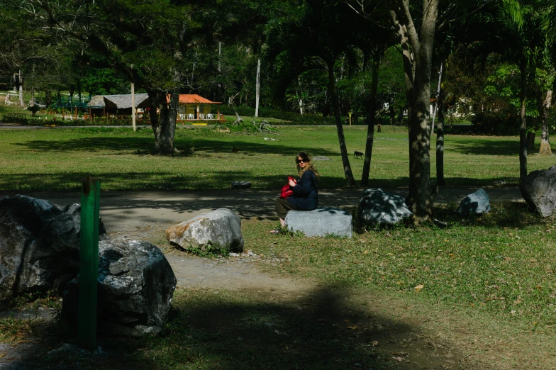 a woman sits on the grass near rocks in a park