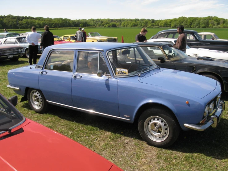 a group of people standing around some blue cars