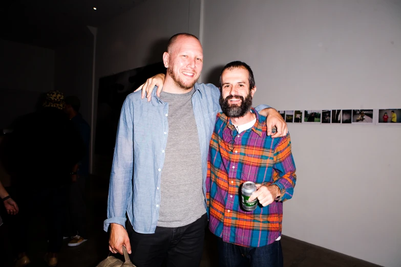 two men pose together in front of some art on the wall