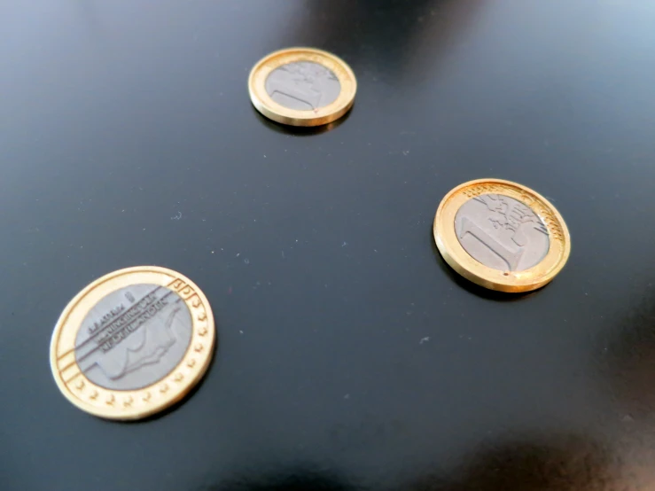 three small gold and silver coins sitting on top of a black surface
