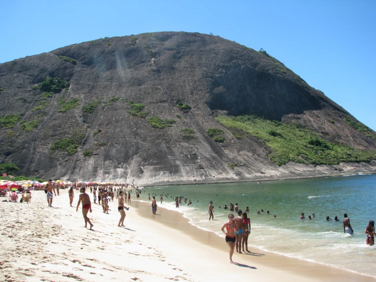 people walking along the beach near some hills