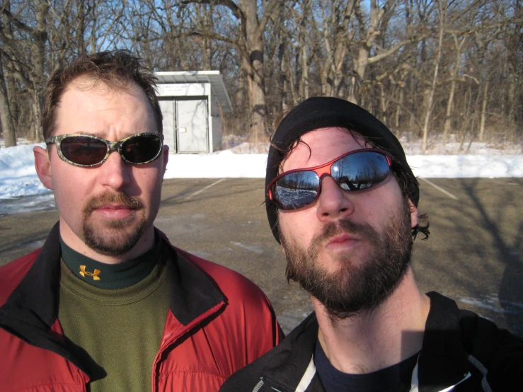 two men in sunglasses standing outside by trees