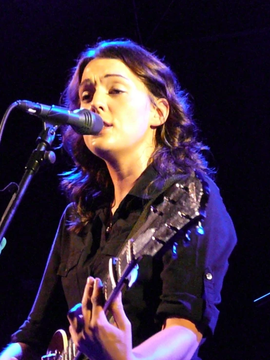 a female with a guitar on stage with microphone
