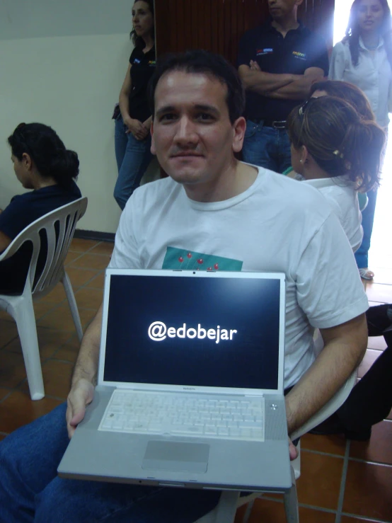 a man is sitting in front of a crowd and holding a laptop
