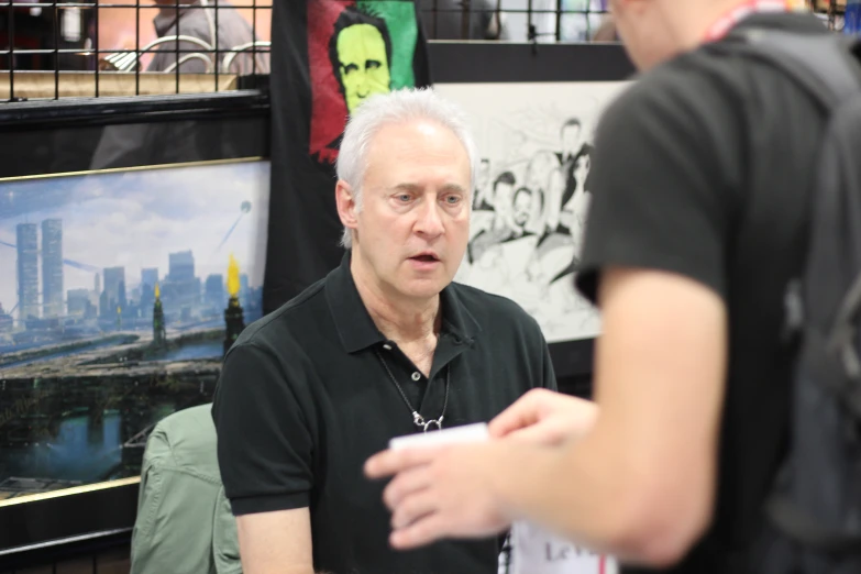 a balding man with a black shirt talks with a lady at an art fair