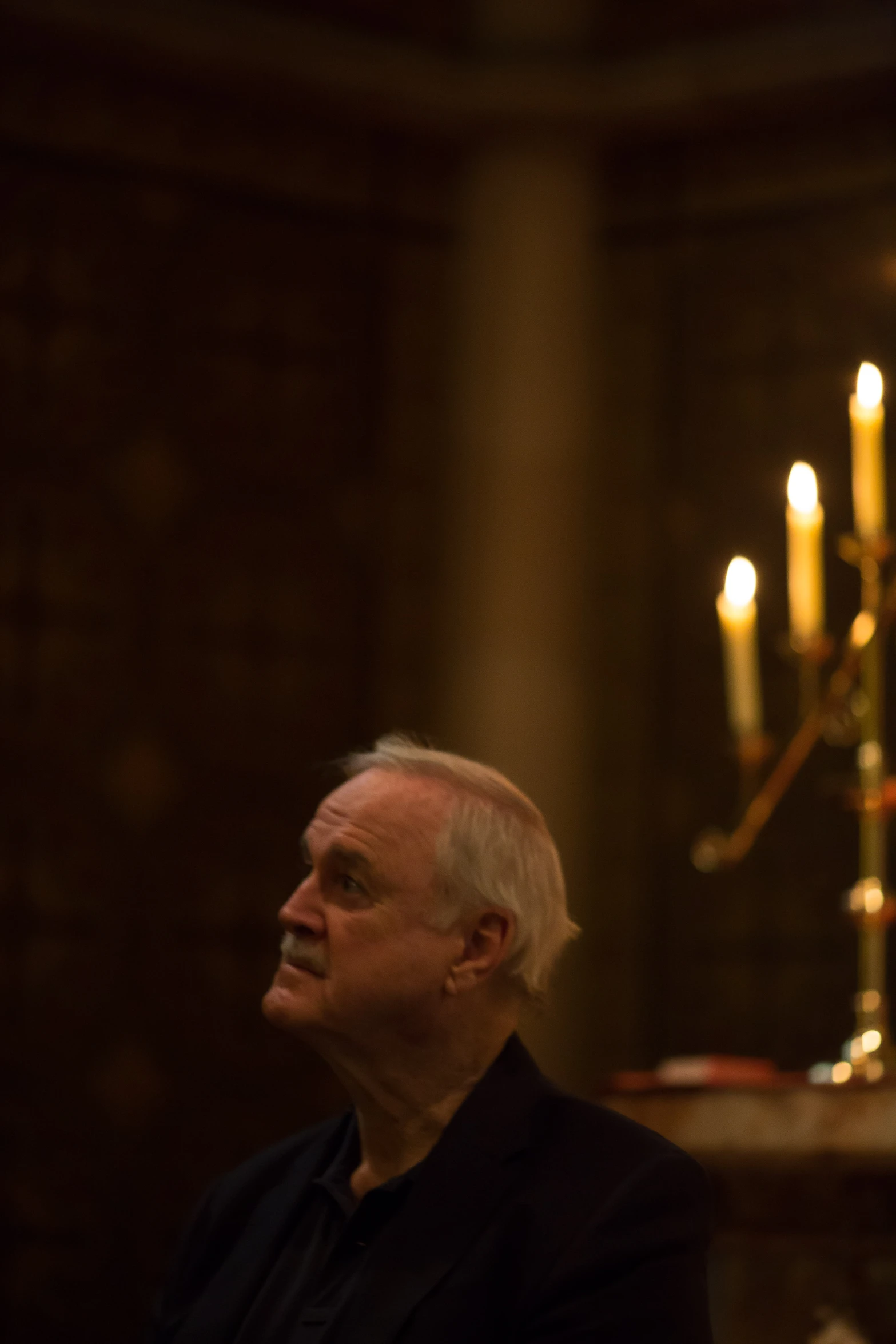 a man sitting down in a chair with two lit candles behind him