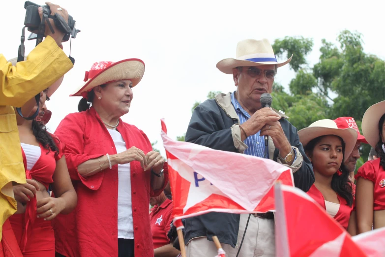 people are taking pos of the parade while a man wearing red is in the microphone