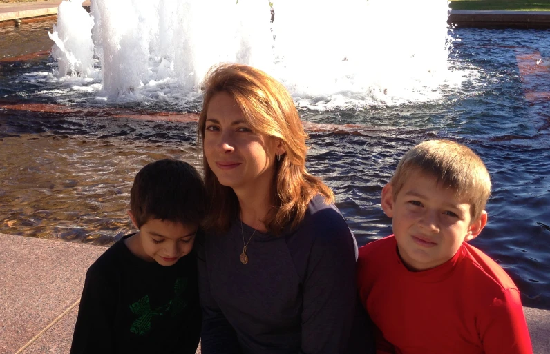 two children are standing next to a woman by the water