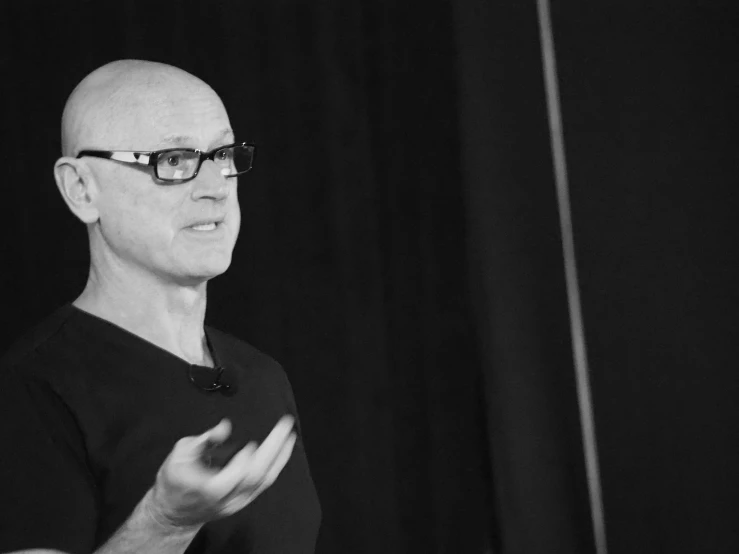 man with black hair and glasses holding his hands in front of him