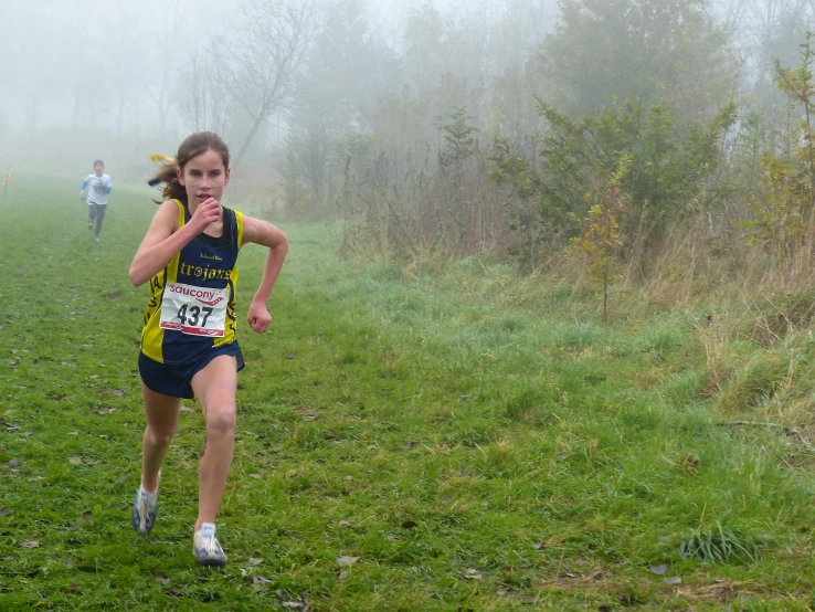 girl in yellow shirt racing on grass next to forest