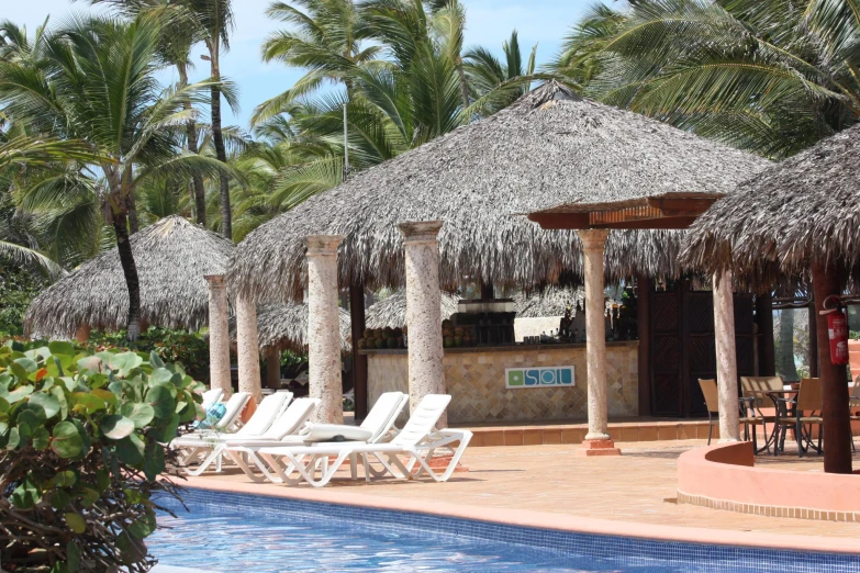 two white chairs sitting under straw thatched roofs near the pool