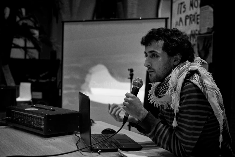 a man in striped sweater speaking on a microphone next to a laptop