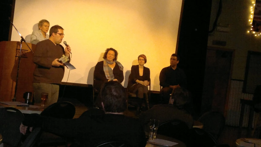 a group of people sitting in front of a microphone in front of a screen