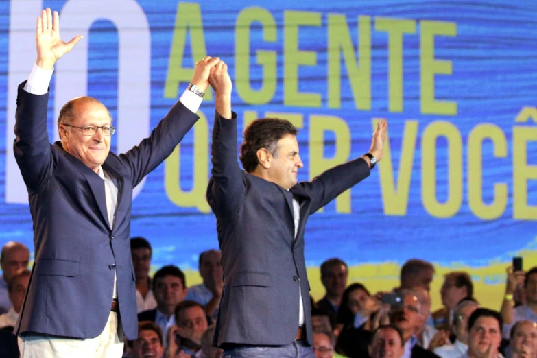 two men in suits are waving on stage
