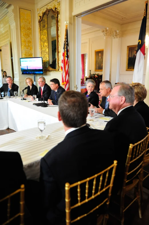 group of men sitting around a white table talking