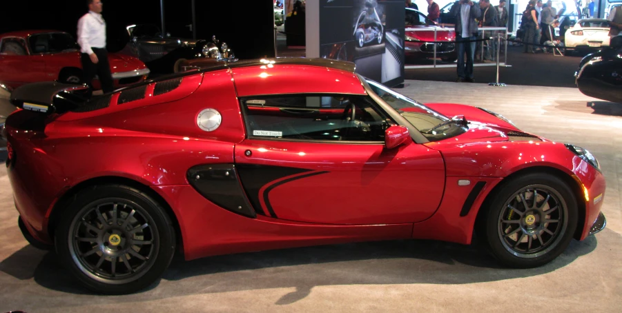 a red car sits on display with people standing around