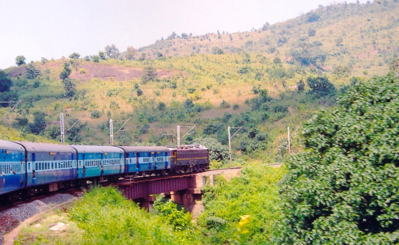 a blue train riding along a lush green hillside
