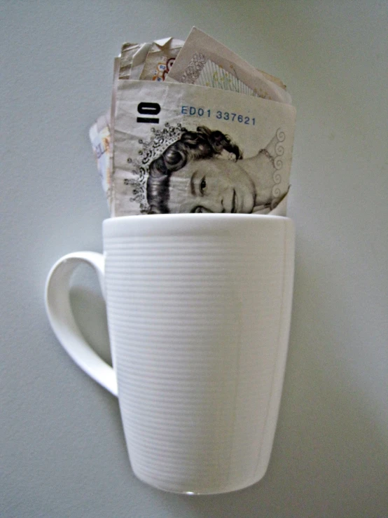 this is a coffee cup with bank notes sticking out of it