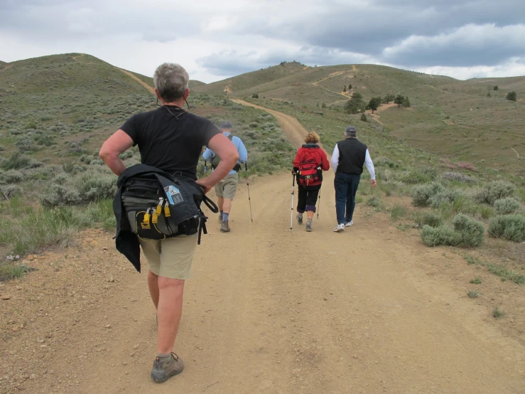 four people walking in the dirt carrying luggage