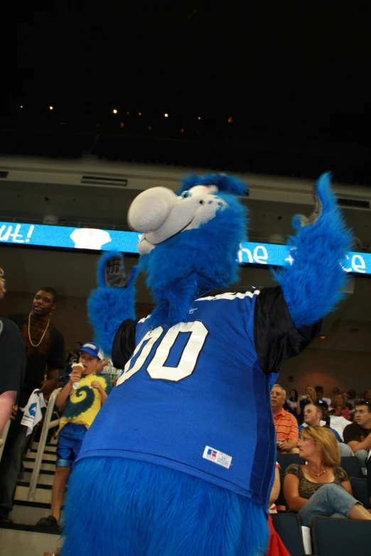 a blue mascot with a large shirt standing in front of an audience