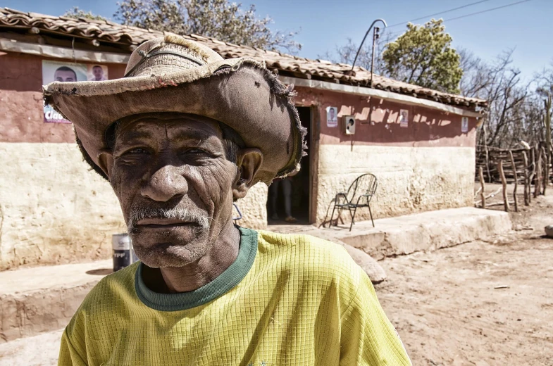 an old man wearing a large hat and standing outside of his home